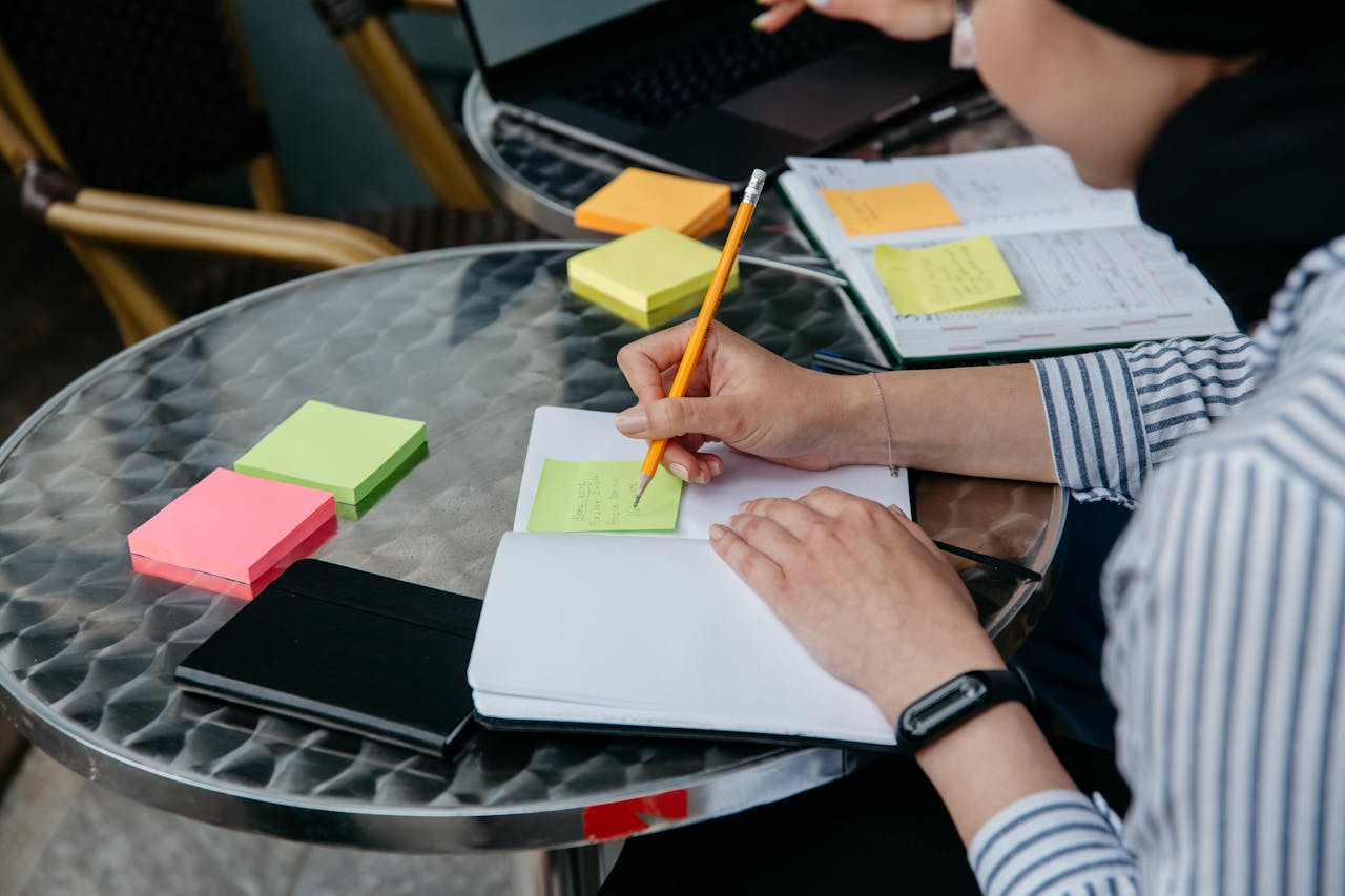 A close-up of hands writing notes on colorful sticky pads at a table.